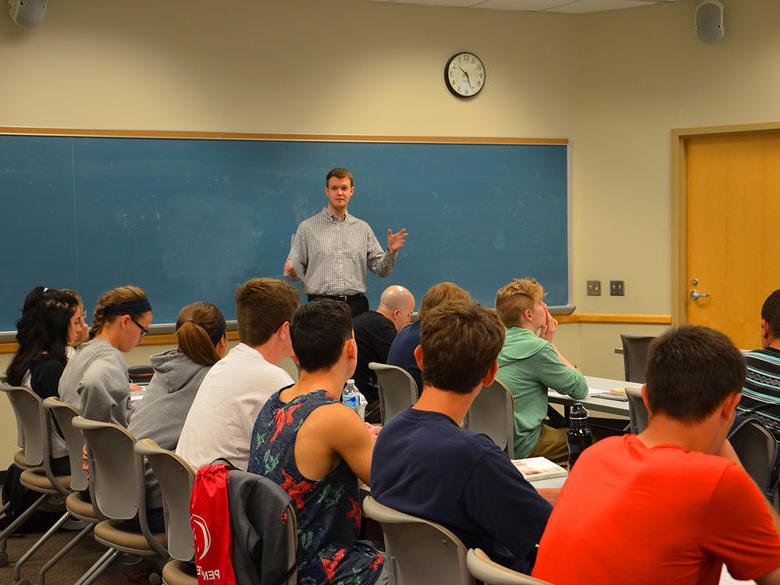 A faculty member stands in front of a chalkboard while teaching to a class of students